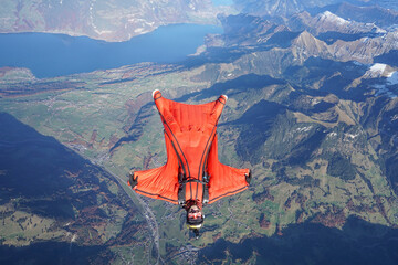 Wingsuit flier glides on his back over snowcapped mountains