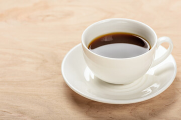 White cup with a beverage on a saucer on a wooden table.