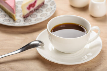White cup with a beverage on a saucer on a wooden table on a background of pieces of cake.