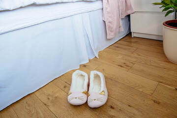 Female or child pink comfort slippers on the wooden floor near the bed. Funny home kitty slippers. Morning habits. Selective focus, copy space.