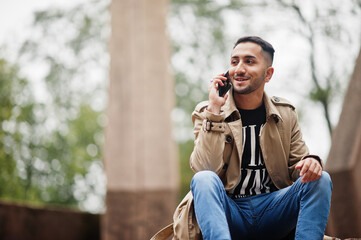 Stylish kuwaiti man at trench coat with mobile phone.