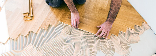 worker installing oak herringbone parquet floor during home improvement - 402885743