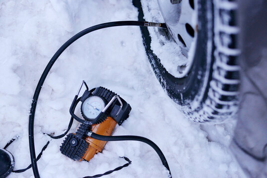 car pump compressor pumps up a flat tire of a car in winter on a snowy path in the forest close-up. Broken cars concept.