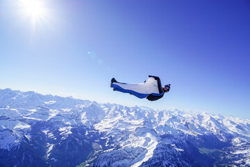 Naklejka na ściany i meble Wingsuit flier glides on his back over snowcapped mountains