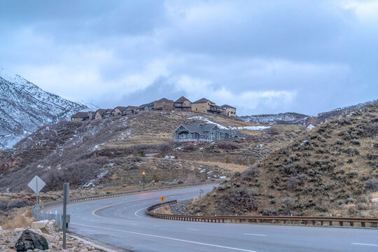 Highway road curving amid mountain with houses on the slope against cloudy sky