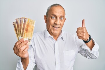 Handsome senior man holding 500 norwegian krone banknotes smiling happy and positive, thumb up...