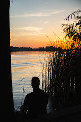 Fototapeta premium sunset and burning sun over the river and a man looking beyond the horizon