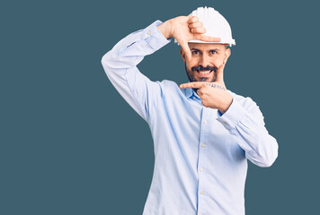 Young handsome man wearing architect hardhat smiling making frame with hands and fingers with happy face. creativity and photography concept.