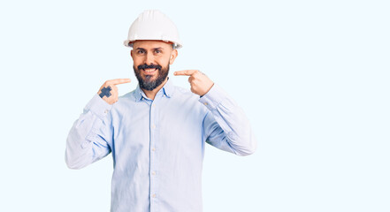 Young handsome man wearing architect hardhat smiling cheerful showing and pointing with fingers teeth and mouth. dental health concept.