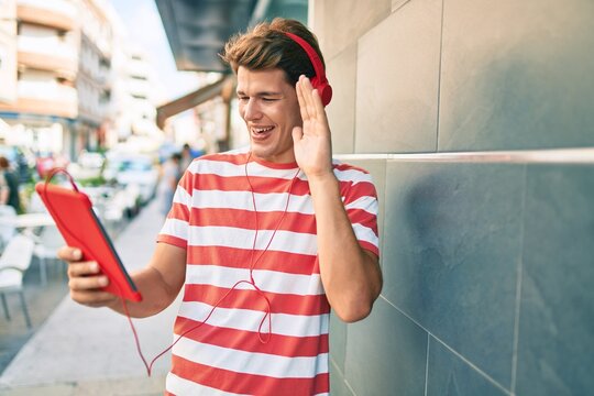 Young caucasian man smiling happy doing video call using touchpad and headphones at the city.