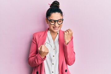 Beautiful middle eastern woman wearing business jacket and glasses celebrating surprised and amazed for success with arms raised and eyes closed. winner concept.