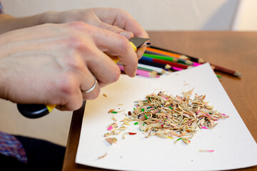 A man sharpens a pencil with a stationery knife