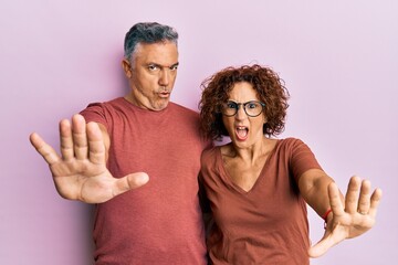 Beautiful middle age couple together wearing casual clothes doing stop gesture with hands palms, angry and frustration expression