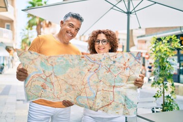 Middle age couple on vacation smiling happy holding map at street of city.