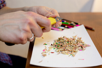A man sharpens a pencil with a stationery knife