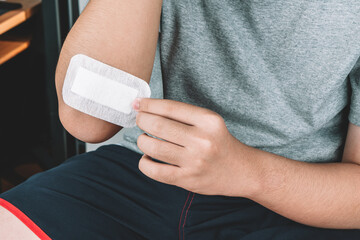 Asian boy putting sticking plaster on injured elbow skin by himself. First aid for cuts and wounds....