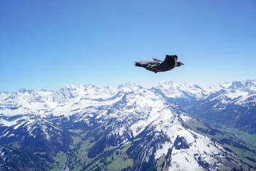 Fototapeta na wymiar Wingsuit flier glides over snowcapped mountains