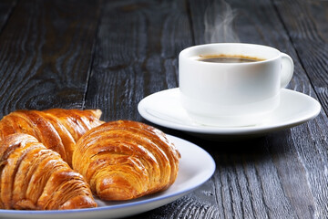 A cup of hot coffee and croissants on a wooden background. Breakfast with coffee and fresh pastry. Copy space. Fresh cake and pastry