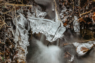 Close up of icicles near wild stream.Snowy winter scenery.Icicle in nature ice background.Cold slippery seasonal weather. Row of frosty icicles.Background of mountain river long exposure water
