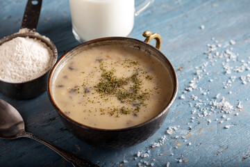 Mushroom cream soup in bowl with glass of milk on wooden background.