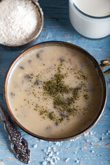 Mushroom cream soup in bowl with glass of milk on wooden background.