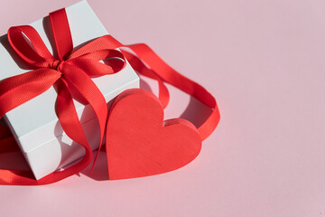 white Gift box with red bow ribbon and red heart on pink background for Valentines day.Happy birthday, wedding, greeting card, love symbol.display of feelings