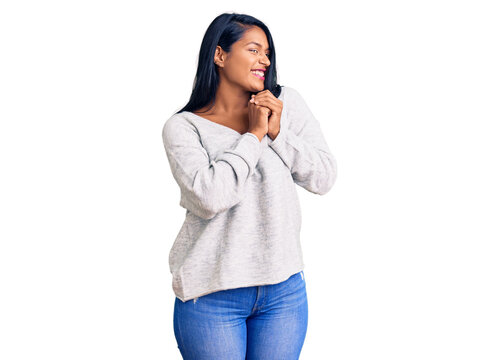 Hispanic woman with long hair wearing casual clothes laughing nervous and excited with hands on chin looking to the side