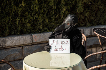 plague doctor holds a sign saying wash your hands