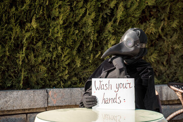 plague doctor holds a sign saying wash your hands