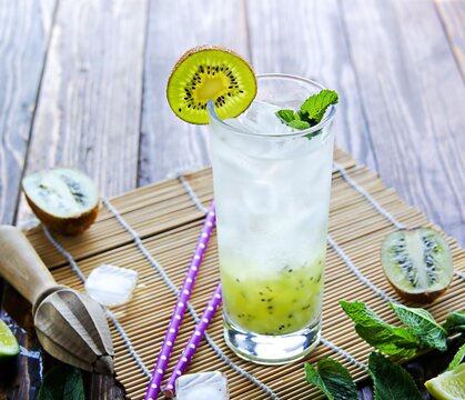 Soft drink, non-alcoholic cocktail with kiwi, lime juice, sparkling water and ice in a tall glass on a wooden background.