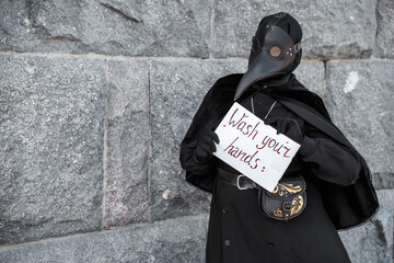 plague doctor holds a sign saying wash your hands