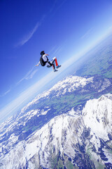 Naklejka na ściany i meble Skydiver performs stunts above snowcapped mountains