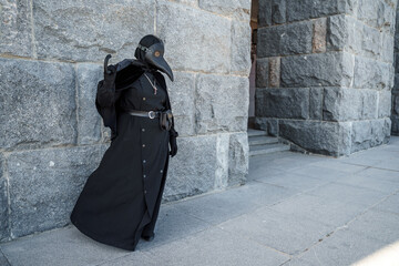 plague doctor stands against a stone wall