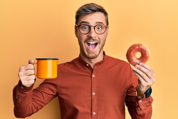 Handsome caucasian man eating doughnut and drinking coffee celebrating crazy and amazed for success...
