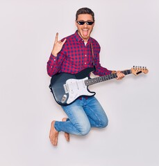 Young hispanic artist man wearing thug life sunglasses with open mouth and tongue out. Jumping with...