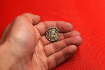 Old coin from India in hand on red background