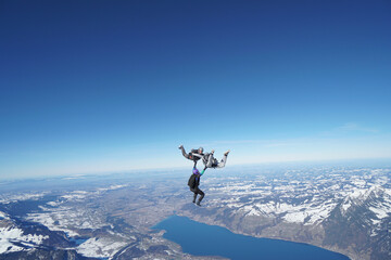 Naklejka na ściany i meble Skydivers perform stunts above snowcapped mountains