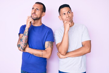 Naklejka premium Young gay couple of two men wearing casual clothes serious face thinking about question with hand on chin, thoughtful about confusing idea