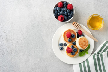 Cottage cheese fritters with summer berries and honey. Top view, grey concrete background with copy space