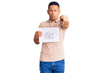 Young handsome latin man holding scribble draw pointing with finger to the camera and to you,...