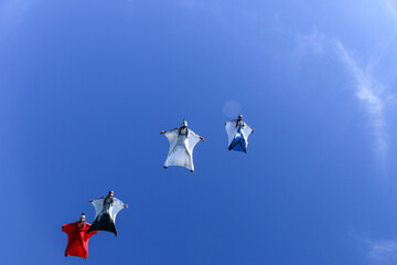 Wingsuit fliers glide in formation, under view to sky above