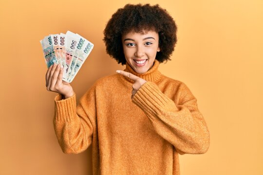 Young hispanic girl holding czech koruna banknotes smiling happy pointing with hand and finger
