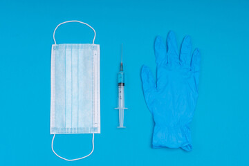 Popular medical antiviral mask, a syringe with a virus vaccine and medical gloves on a blue background