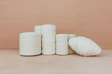 Fototapeta na wymiar Set of white knitting yarn spool on beige background. Different size cotton threads. 