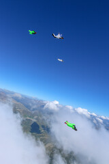 Wingsuit fliers glide in formation above lofty clouds