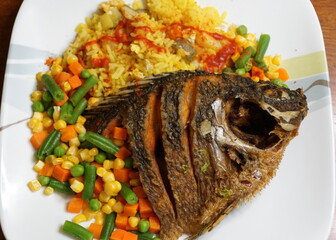 Fried tilapia with yellow rice and mixed vegetable on a white plate