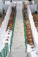 Concrete stairs with green handrails amid snowy yards and white wooden fences