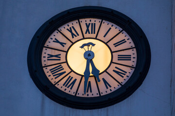 Grande orologio illuminato, con i numeri romani, di antico campanile bianco. Fotografia notturna.