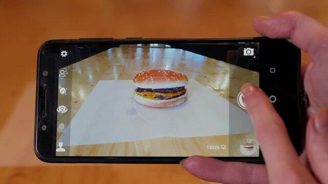 Women's hands take pictures on a mobile phone of a burger with beef patty with melted cheese.