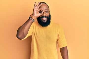 Young african american man wearing casual clothes doing ok gesture with hand smiling, eye looking through fingers with happy face.